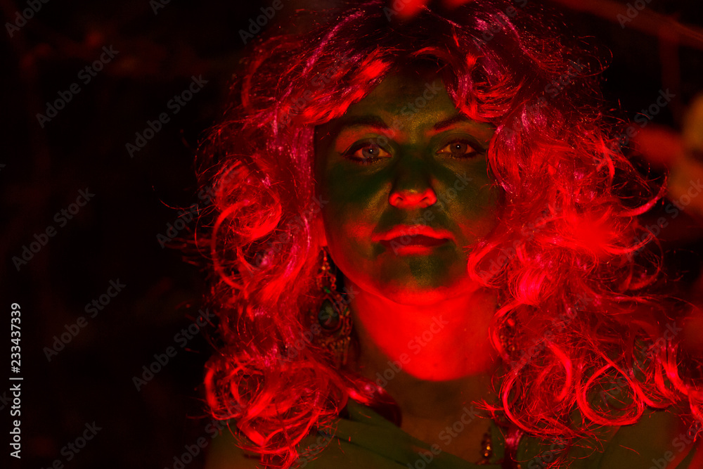 The face of the woman of the forest witch is a close-up in the gleam of red light. Light falls on the face.