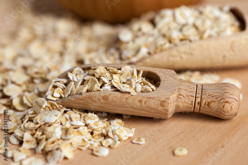 Oat flakes in a wooden bowl with a scoop on the wooden board