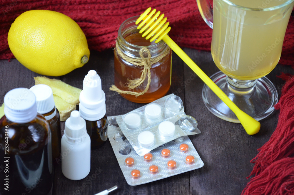 healthcare, traditional medicine and flu concept - tea cup with lemon, ginger, honey and pills on wooden table. tablets, pills, cough syrups, nasal drops and non-traditional alternative medicine. healthcare, traditional medicine and flu concept - tea cup with lemon, ginger, honey and pills on wooden table. tablets, pills, cough syrups, nasal drops and non-traditional alternative medicine.