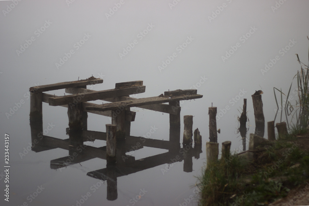 Old broken bridge over the lake in the morning fog .