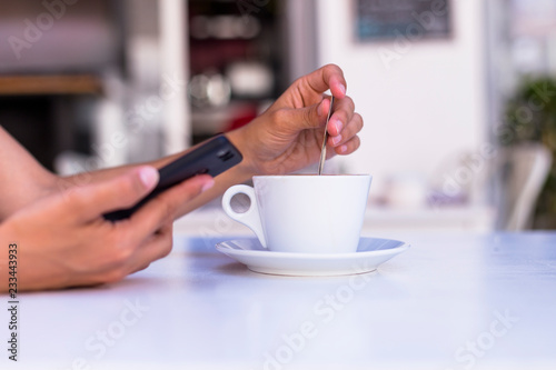 close up view of woman hands holding a cup of coffee and mobile phone in a terrace. Morning, daytime and technology