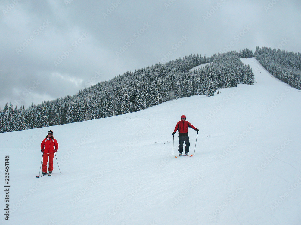 Two skiers, a man and a woman, in red clothes at the foot on a ski Track in mountainside.