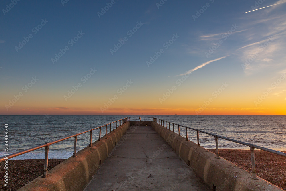 Looking down a jetty out to sea, with a sunset sky behind