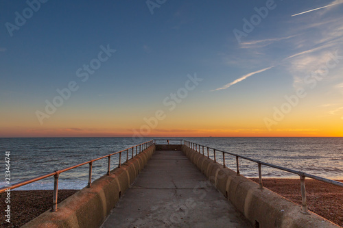 Looking down a jetty out to sea  with a sunset sky behind