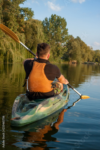 Young bearded man sitting with paddle in kayak near the coast of the lake