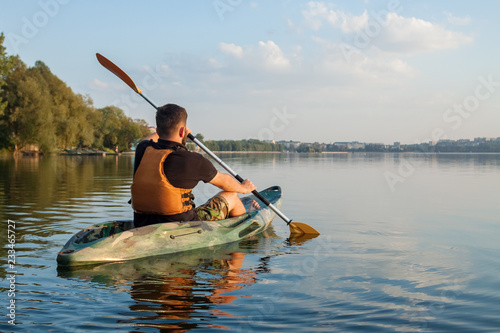 Young bearded man paddling in kayak in the middle of the lake from the back