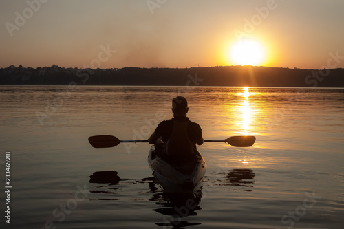 A man with paddle having a rest in kayak silhouette in sunset