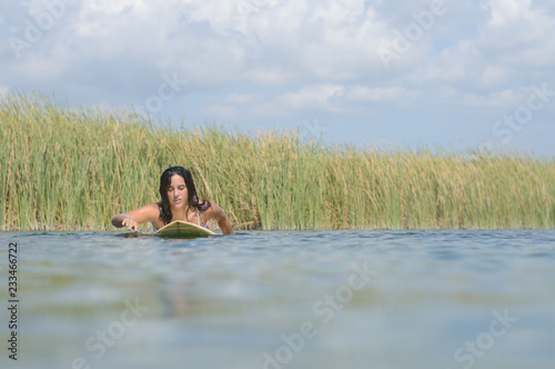 young caucasian woman swimming on a surfboard