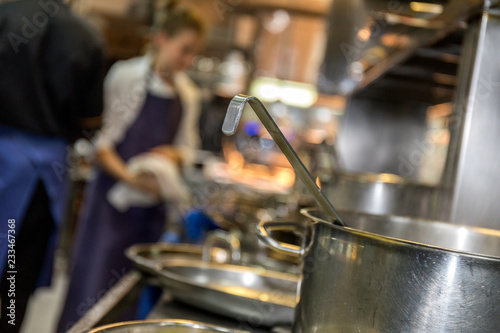 Fototapeta Naklejka Na Ścianę i Meble -  People in the kitchen of a restaurant with a cooking pot in the foreground 