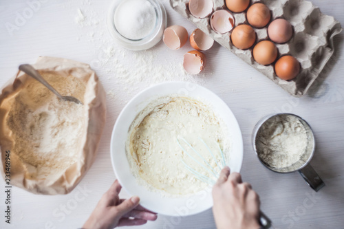 Process of making the dough, woman's hand whips eggs and flour in bowl Flat lay composition of ingredients and batter.selective focus