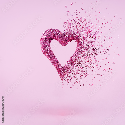 Glitter heart dissolving into pieces on pink background. Valentines day, broken heart and love emergence concept