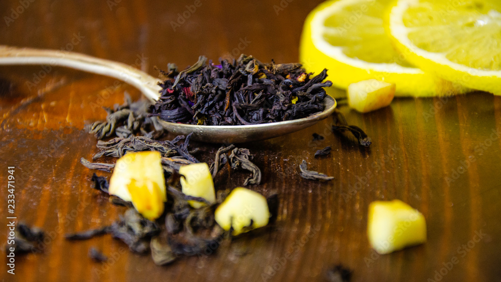 Dry tea leaves in a teaspoon, lemon, wooden table Dry tea leaves in a teaspoon, lemon, wooden table
