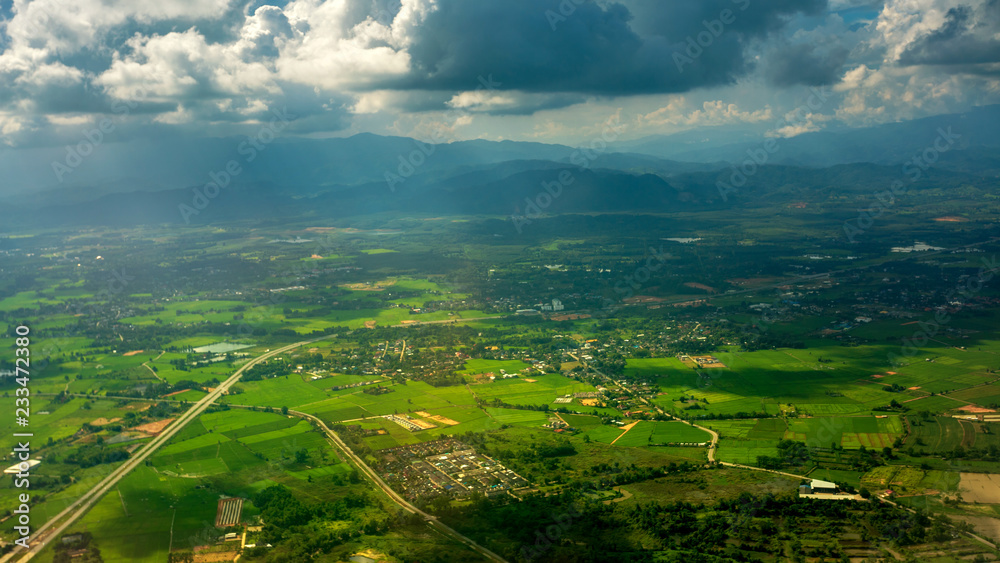 Sunbeam passing through the cloud over Chiangrai city with green grass field and mountain range. the areal shot has been taken through Airplane window.