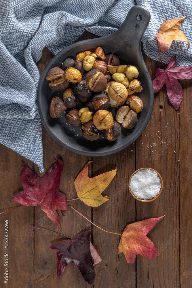 Roasted chestnuts in cast iron grilling pan over rustic wooden board.
