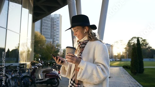 Beautiful woman in the hat with earphone drinking coffe and chatting on the smart phone. photo