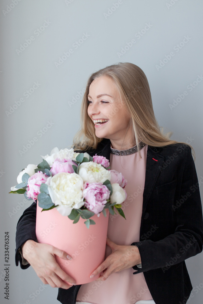 Charming blonde woman with flowers in a hat box. Bouquet of peonies. Girl in business style, receives flowers or gives
