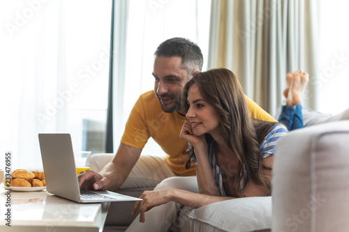 Couple in love are sitting on sofa and watching gadget. Copy space on left side