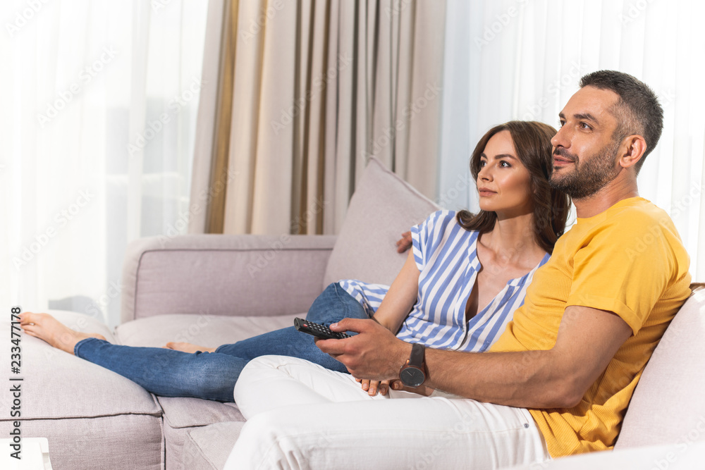 Fine weekend. Beautiful woman and smiling man is watching TV in their light flat. Copy space in left side