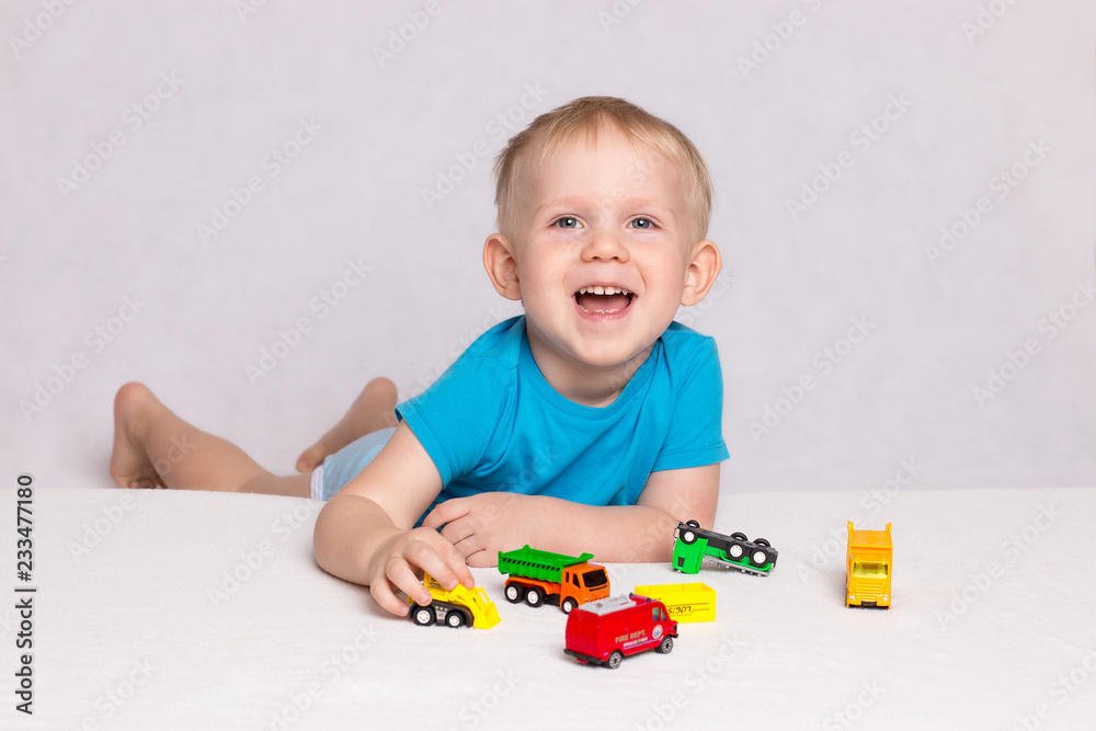 Little happy blond boy playing colored cars on white background Little happy blond boy playing colored cars on white background