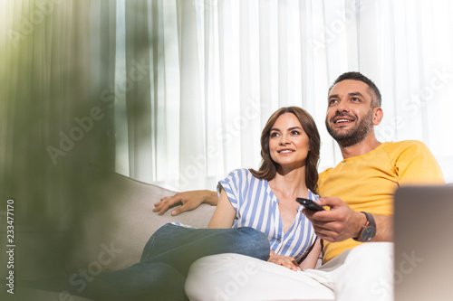 Loving man and woman is sitting on couch and watching TV at home/ Copy space in left side