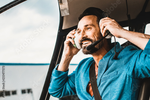 Close up of a happy young man wearing big headphones while sitting in the helicopter and smiling