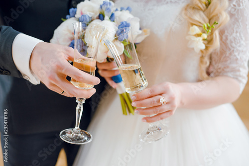 The bride and groom hold glasses of champagne in their hands on wedding celebration. Close up. Wedding ceremony.