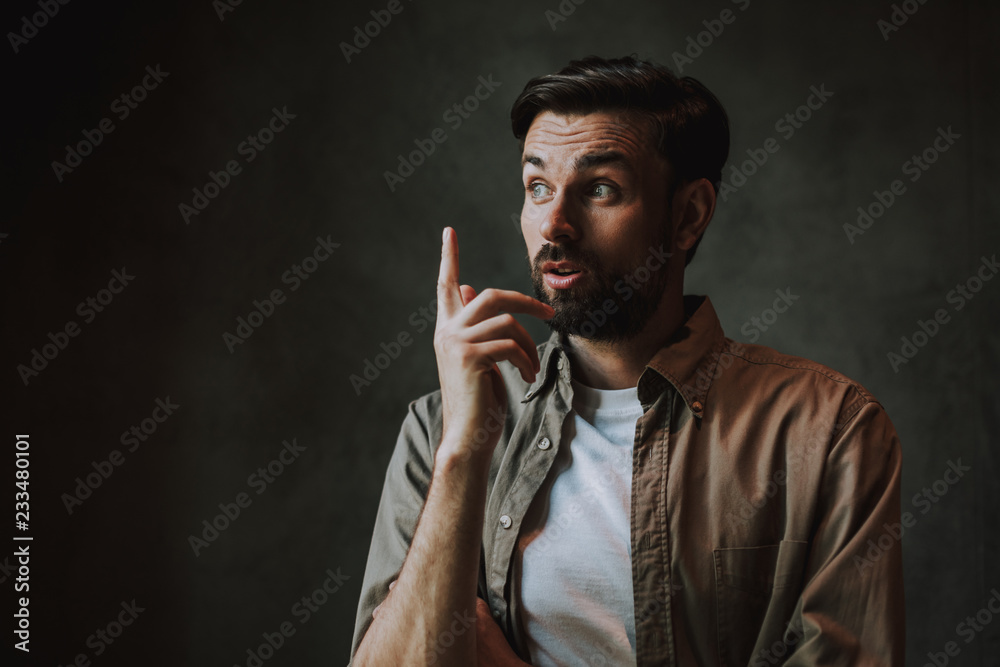Portrait of thoughtful bearded man gesticulating hand while having interesting idea. He isolated on dark background
