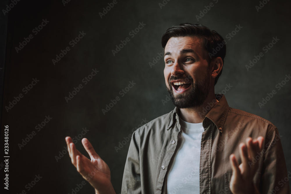 Portrait of outgoing bearded man with attractive smile gesticulating hands while expressing happiness