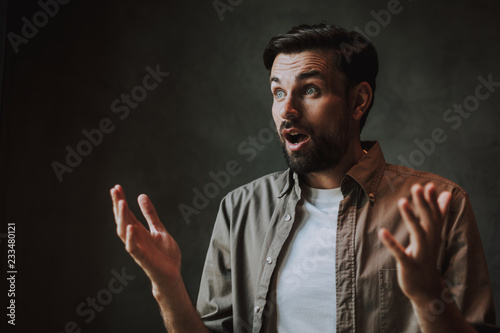 Portrait of surprised man with open mouth flourishing arms while grimacing face