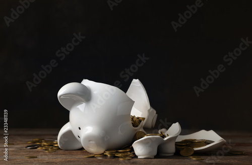 Broken piggy bank with money on table against dark background