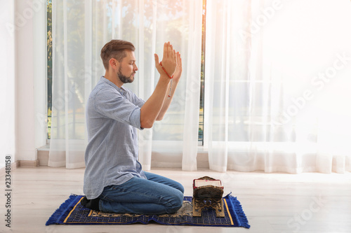 Canvas Print Muslim man with Koran praying on rug indoors