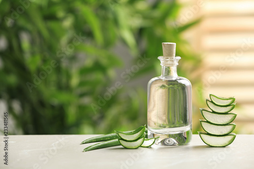 Bottle with aloe vera juice and slices of fresh leaves on table against blurred background. Space for text