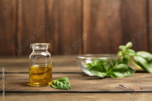 Glass bottle of basil oil and leaf on wooden table. Space for text