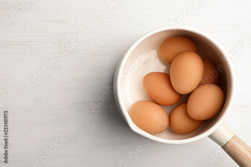 Saucepan with boiled eggs on wooden background, top view. Space for text