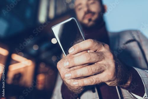 Calm man standing alone and looking at the screen of his gadget while holding it