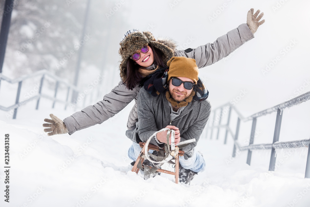 Young happy couple riding sled in snow - obrazy, fototapety, plakaty 