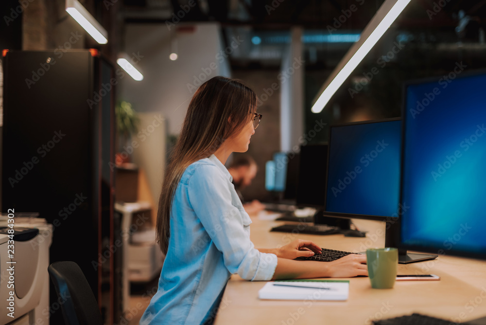Side view portrait of beautiful women using keyboard and mouse while sitting at desk and looking at PC monitor Side view portrait of beautiful women using keyboard and mouse while sitting at desk and looking at PC monitor