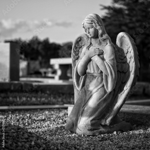 Black and white image of an angel statue in a cemetery.