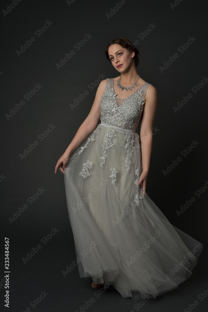 full length portrait of brunette girl wearing long silver ball gown. standing pose on grey studio background. full length portrait of brunette girl wearing long silver ball gown. standing pose on grey studio background.
