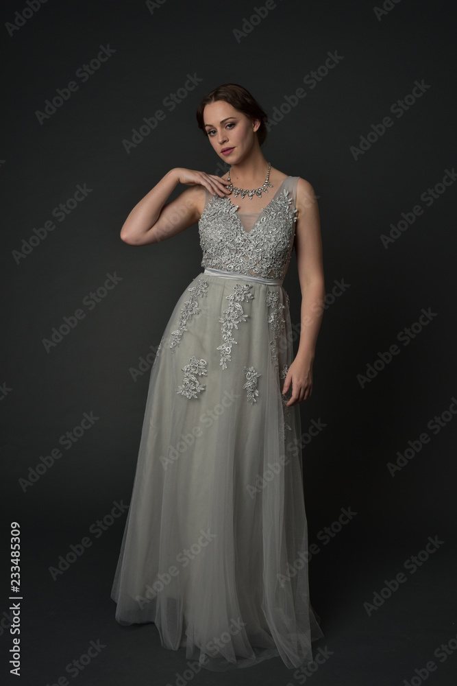 full length portrait of brunette girl wearing long silver ball gown. standing pose on grey studio background. full length portrait of brunette girl wearing long silver ball gown. standing pose on grey studio background.
