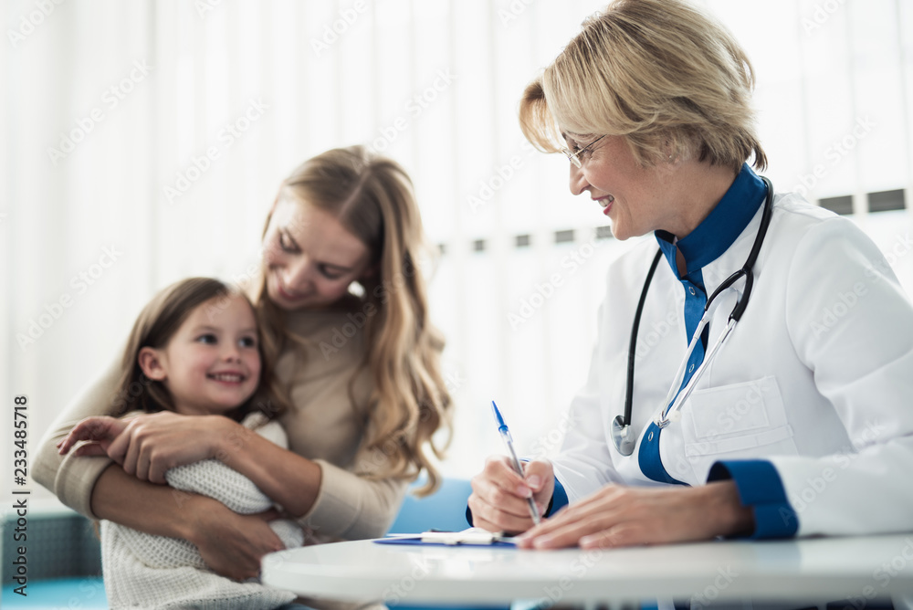 Concept of trustworthy method of consultation in healthcare system. Waist up portrait of smiling little girl and her mother visiting pediatrician in medical cabinet Concept of trustworthy method of consultation in healthcare system. Waist up portrait of smiling little girl and her mother visiting pediatrician in medical cabinet