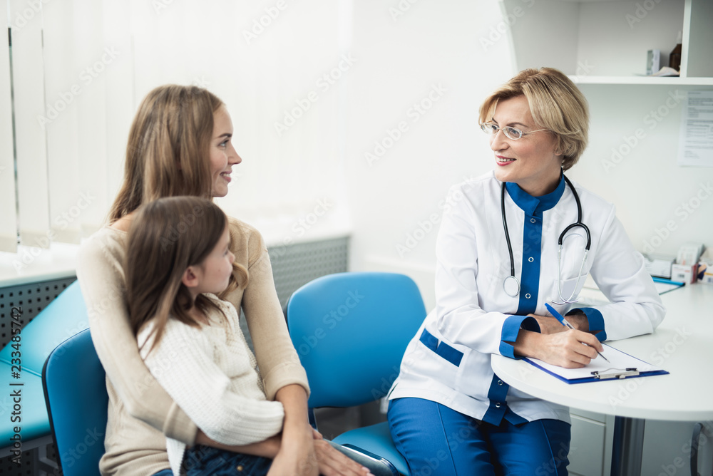 Concept of positive method of consultation in healthcare system. Waist up portrait of smiling little girl and her mother consulting in pediatrician cabinet
