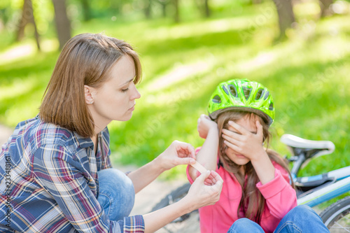 Mother puts a bandage on a wound to little girl  who fell off his bicycle. Focused on hands