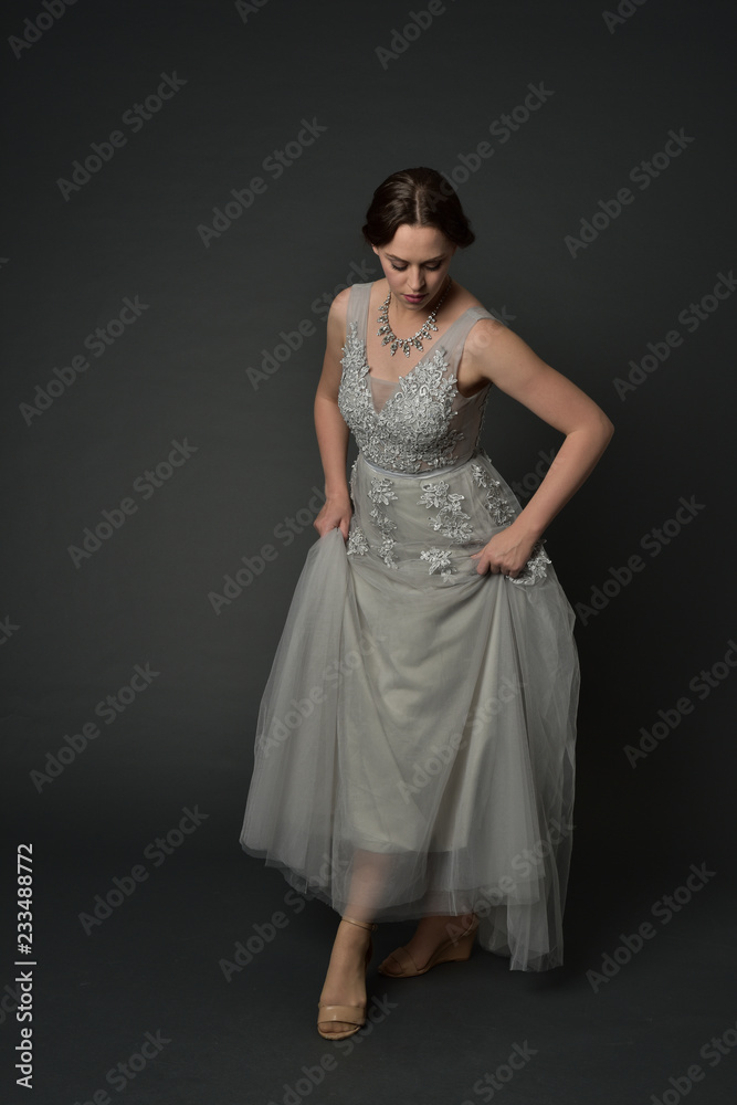 full length portrait of brunette girl wearing long silver ball gown. standing pose on grey studio background. full length portrait of brunette girl wearing long silver ball gown. standing pose on grey studio background.