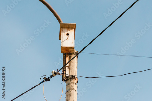 Lamppost with wooden birdhouse. Wires for electricity in the lantern. Blue sky