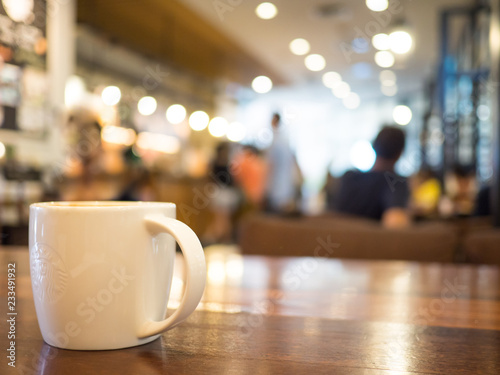 Chiang mai, Thailand-September 22,2018: Hot coffee cappuccino in white cup starbucks on wooden table and blurred background cafe stores. photo