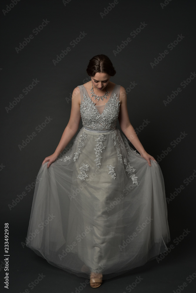 full length portrait of brunette  girl wearing long silver ball gown. standing pose on grey studio background.