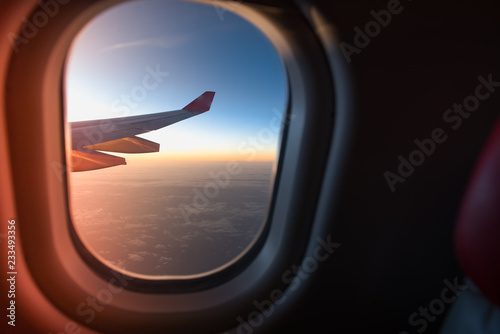 View from the window of airplane wing while fly over the blue sky with sea of clouds in twilight time.