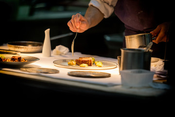Chef preparing a dish with meat on a plate under a light. The chef is meticulous. 