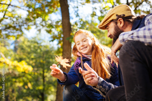 Autumn season. Cute red haired girl holding an orange leaf while sitting together with her dad photo